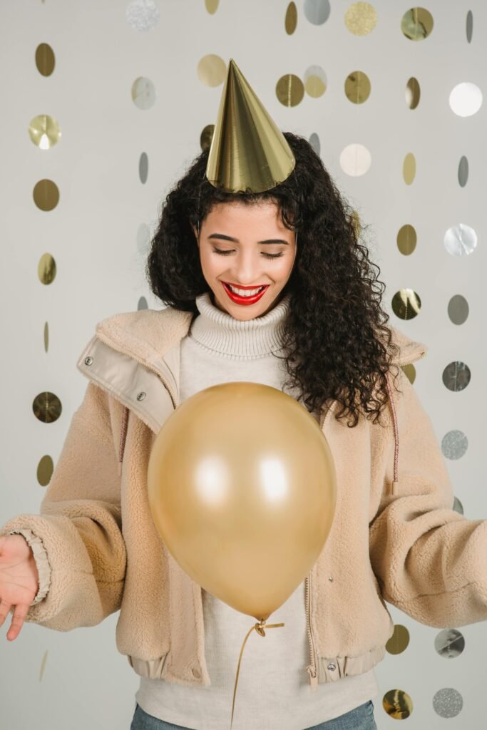 pexels-photo-6113627-6113627 A happy woman in winter clothing celebrating indoors with a gold balloon.